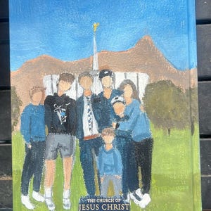 May include: Hand-painted artwork showing a family in front of a white building with a gold spire, set against a blue sky and green grass. The text "THE CHURCH OF JESUS CHRIST OF LATTER-DAY SAINTS" is visible.