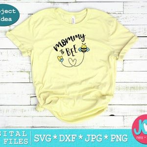 May include: A yellow t-shirt with the text "mommy to bee" in black lettering. A small bee with black and yellow stripes and blue wings is above the text. Two blue and yellow hearts are below the text with a dotted line connecting them to the bee.