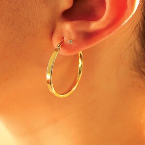May include: A close-up of a person's ear with a gold hoop earring. The earring is simple and elegant, with a smooth, polished finish.