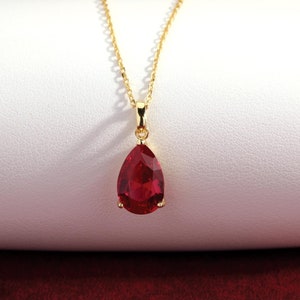 May include: A gold chain necklace with a teardrop-shaped red gemstone pendant.