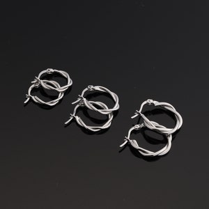 May include: A collection of silver-colored hoop earrings. The earrings have a twisted rope design. The earrings are displayed on a black surface. The earrings are available in multiple sizes.