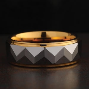 May include: A black and gold tungsten carbide ring with a faceted design.
