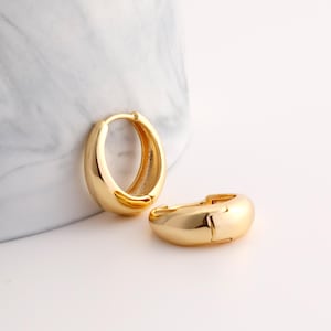 May include: A pair of gold hoop earrings. The earrings are thick and have a rounded shape.