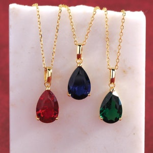 May include: Three gold necklaces with teardrop-shaped pendants. The pendants are red, blue, and green.