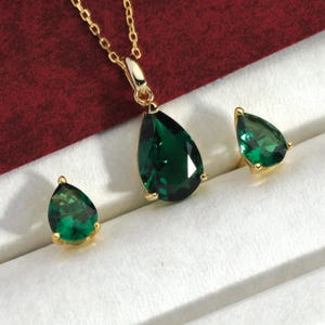 May include: A gold necklace with a teardrop-shaped emerald pendant and matching earrings. The earrings are also teardrop-shaped with emerald stones.