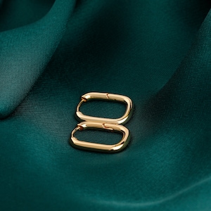 May include: A pair of gold oval hoop earrings on a green fabric background.
