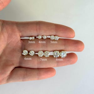 K&ouml;nnte beinhalten: Eine Auswahl an goldenen Ohrsteckern mit klaren, runden Edelsteinen. Gr&ouml;&szlig;en von 3 mm bis 8 mm, auf dem Bild beschriftet. Die Ohrringe werden auf hellem Hintergrund pr&auml;sentiert, um ihr Funkeln und die verschiedenen Gr&ouml;&szlig;en hervorzuheben.