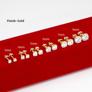 K&ouml;nnte beinhalten: Eine Auswahl an goldfarbenen Ohrsteckern mit klaren, runden Zirkonia-Steinen. Gr&ouml;&szlig;en von 3 mm bis 8 mm, pr&auml;sentiert auf roter Samtoberfl&auml;che. Der Text "Finish: Gold" ist sichtbar.