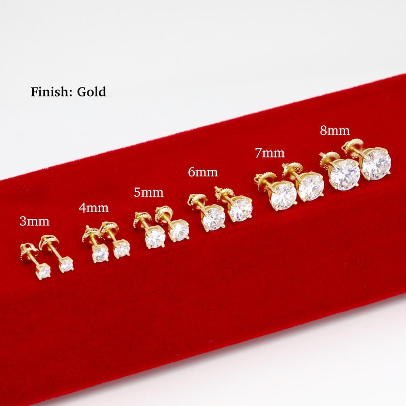 K&ouml;nnte beinhalten: Eine Auswahl an goldfarbenen Ohrsteckern mit klaren, runden Zirkonia-Steinen. Gr&ouml;&szlig;en von 3 mm bis 8 mm, pr&auml;sentiert auf roter Samtoberfl&auml;che. Der Text "Finish: Gold" ist sichtbar.