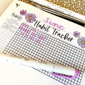 May include: A June habit tracker with a grid of squares for each day of the month. The grid is filled with pink and purple squares to mark completed habits. The words "June Habit Tracker" are written in cursive at the top of the grid. The words "Habits" are written in cursive at the left of the grid, followed by a list of habits: Gym, Meditate, H2O, Gam Wake Up, Read, Make Bed.