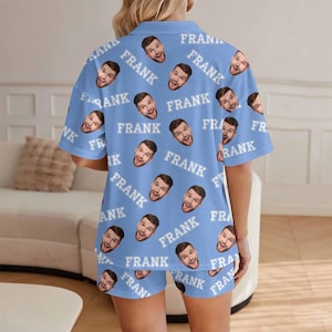 K&ouml;nnte beinhalten: Hellblaues Pyjama-Set mit einem sich wiederholenden Muster eines l&auml;chelnden Gesichts und dem Namen "FRANK" in Wei&szlig;. Das Set beinhaltet ein kurz&auml;rmeliges Hemd mit Kn&ouml;pfen und passende Shorts, ideal als personalisiertes Geschenk.