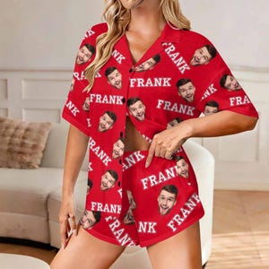 K&ouml;nnte beinhalten: Rotes Pyjama-Set mit einem sich wiederholenden Muster eines l&auml;chelnden Gesichts und dem Namen "FRANK" in Wei&szlig;. Das Set beinhaltet ein Hemd mit Kn&ouml;pfen und passende Shorts. Das Hemd hat kurze &Auml;rmel und einen Kragen.
