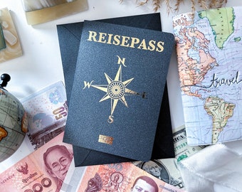 Może przedstawiać: Czarny pokrowiec na paszport z pozłacanym napisem "REISEPASS" i złotym wzorem kompasu. Pokrowiec leży na białym tle z mapą świata, pieniędzmi i globusem.