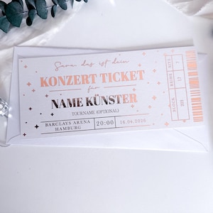 Puede incluir: Una entrada de concierto con texto en oro rosa sobre fondo blanco. La entrada dice "KONZERT TICKET" y "NAME K&Uuml;NSTER" con el lugar y la fecha impresos debajo. La entrada est&aacute; dentro de un sobre blanco, con elementos decorativos.