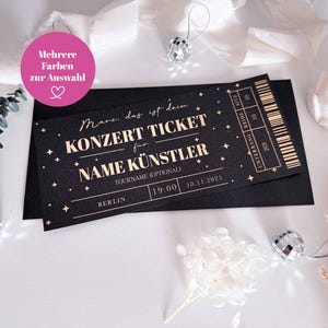 May include: Black concert ticket with gold text and star accents. The ticket reads "KONZERT TICKET" and includes space for the artist's name, tour name, and date. The ticket is on a black envelope with decorative elements.