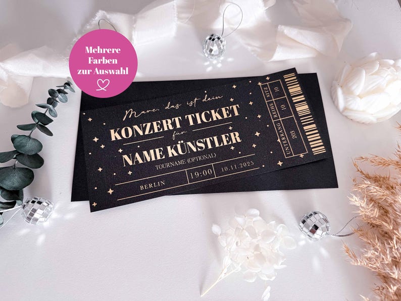 Puede incluir: Entrada de concierto negra con texto dorado y estrellas. La entrada dice "KONZERT TICKET" e incluye espacio para el nombre del artista, el nombre de la gira y la fecha. La entrada est&aacute; sobre un sobre negro con elementos decorativos.