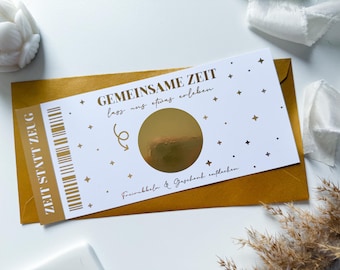 May include: A white card with gold lettering and a gold scratch-off circle. The card says "GEMEINSAME ZEIT lass uns etwas erleben." and "Freirubbeln & Geschenk entdecken".