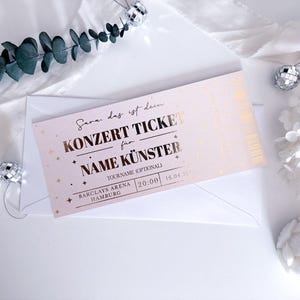 Puede incluir: Un boleto de concierto rosa con letras doradas, dentro de un sobre blanco. El boleto dice "KONZERT TICKET" y "NAME K&Uuml;NSTER". Elementos decorativos incluyen bolas de discoteca y vegetaci&oacute;n.