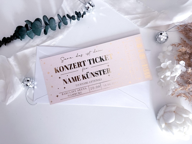 Puede incluir: Un boleto de concierto rosa con letras doradas, dentro de un sobre blanco. El boleto dice "KONZERT TICKET" y "NAME K&Uuml;NSTER". Elementos decorativos incluyen bolas de discoteca y vegetaci&oacute;n.