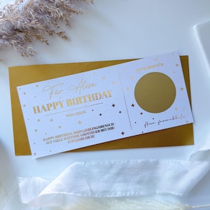 Könnte beinhalten: Goldfolien-Geburtstagskarte mit dem Text "Happy Birthday" und "Far Alisa" in eleganter Schrift. Die Karte enthält einen Rubbelkreis und liegt auf einem goldenen Umschlag. Dekorative Elemente sind Sterne.