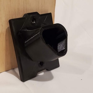 Op de afbeelding: Een zwarte plastic wandbevestiging met een gebogen opening, ontworpen om een apparaat of object vast te houden.