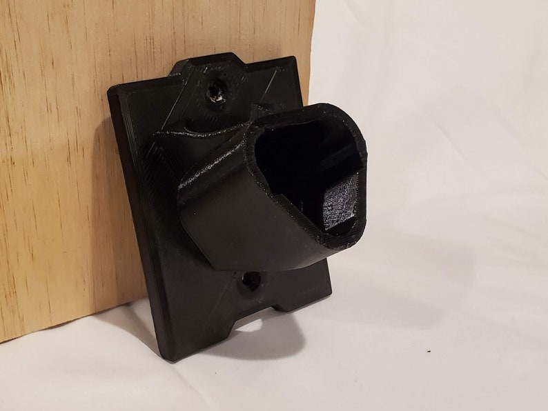 Op de afbeelding: Een zwarte plastic wandbevestiging met een gebogen opening, ontworpen om een apparaat of object vast te houden.