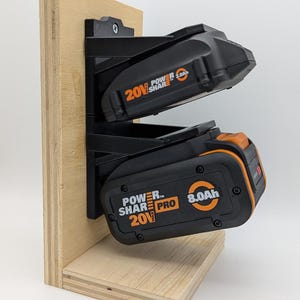 May include: A black battery holder with two slots, mounted on a light-colored wooden base. Two black and orange 20V Power Share Pro batteries are inserted. One battery is labeled 8.0Ah, the other 2.0Ah.