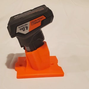 Op de afbeelding: Oranje 3D-geprinte wandbevestiging voor een zwarte Hyper Tough 4,0Ah lithium-ionbatterij. De beugel heeft twee gaten om aan een muur te bevestigen.