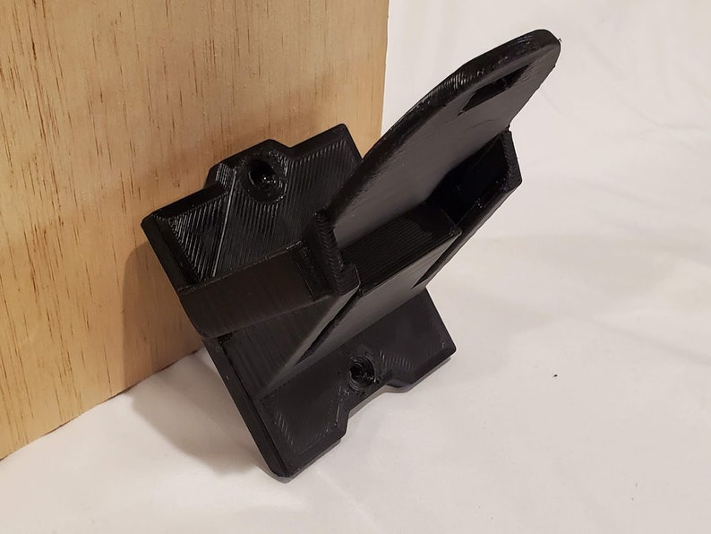 Op de afbeelding: Een zwarte 3D-geprinte wandbeugel met een rechthoekige basis en een gebogen arm die naar boven uitsteekt. De beugel heeft twee schroefgaten op de basis en &eacute;&eacute;n op de arm.