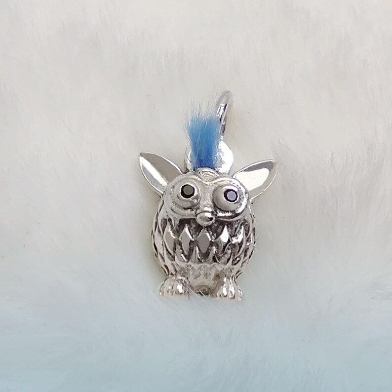 K&ouml;nnte beinhalten: Silberner Anh&auml;nger in Form eines pelzigen Monsters mit einem blauen Irokesenschnitt, schwarzen Augen und einem zahnigen Grinsen.