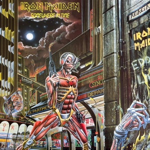Op de afbeelding: Een sciencefiction-albumhoes met een skeletachtige figuur met blootliggende spieren en een robotarm, die een pistool vasthoudt. De figuur staat in een futuristische stadsetting met neonborden en een maan op de achtergrond. De albumtitel "Iron Maiden Somewhere in Time" staat bovenaan.
