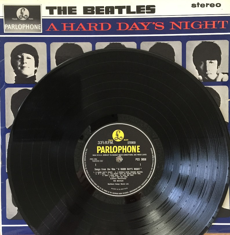 May include: A black vinyl record with a white label. The label has the text "The Beatles" and "A Hard Day's Night" in red and black lettering. The label also has the text "Parlophone" in black lettering and a small image of a pound sign.