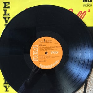 May include: A black vinyl record with the label "Side 2 Stereo" and the text "Rock 'N' Roll" by Elvis Presley. The record is on a yellow background with the word "Elvis" visible.