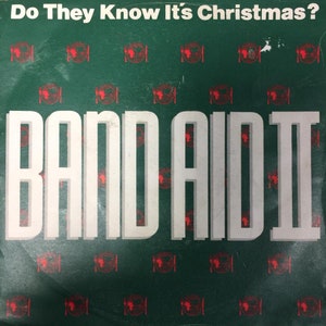 May include: A green vinyl record with the title "Do They Know It's Christmas?" and the text "Band Aid II" in white letters. The record cover has a repeating pattern of red and white logos.