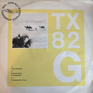 Può includere: Copertina di un disco in vinile con sfondo giallo e la scritta "TX 82 G" in grandi lettere bianche. Un'immagine in bianco e nero di cammelli in un paesaggio desertico si trova nell'angolo in alto a sinistra. Il logo The Teardrop Explodes è nell'angolo in alto a sinistra.