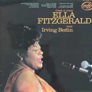 Puede incluir: Una portada de disco de vinilo vintage con una foto en blanco y negro de Ella Fitzgerald cantando. La portada se titula "Cheek to Cheek Ella Fitzgerald canta Irving Berlin".