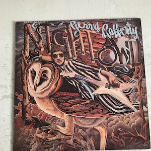 Peut inclure: Une pochette d'album de disque vinyle vintage représentant un homme avec une guitare et un hibou. L'album est intitulé "Night Owl" par Gerry Rafferty.