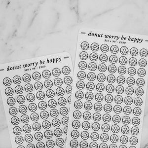 May include: Two sheets of clear sticker paper with black donut illustrations. Each sheet has 98 donuts and the text "donut worry be happy" and "look for something positive in each day".