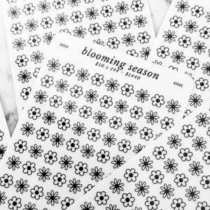 May include: Several sheets of white stickers with a repeating pattern of black daisy-like flowers. The text "blooming season" is printed on one sheet, along with a price range.
