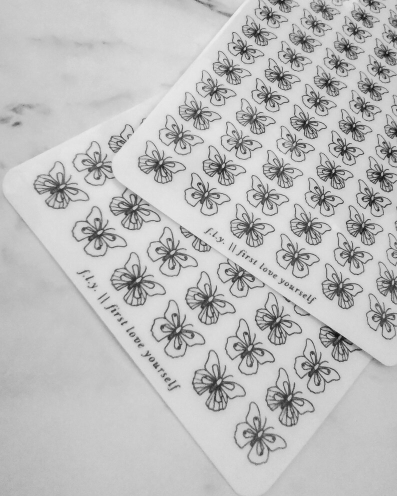 May include: Two sheets of clear sticker paper with black butterfly outlines. The text "fly. || first love yourself" is printed on each sheet.