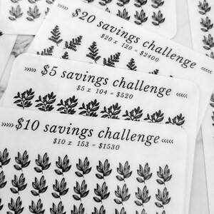 May include: Three white cards with black text and illustrations of leaves. The cards are labelled "&pound;20 savings challenge", "&pound;5 savings challenge", and "&pound;10 savings challenge". Each card has a math equation showing the total savings for each challenge.