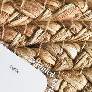 May include: A white card with rounded corners and the text "rounded corners" written on it. The card is lying on a woven, light brown, natural fiber surface.