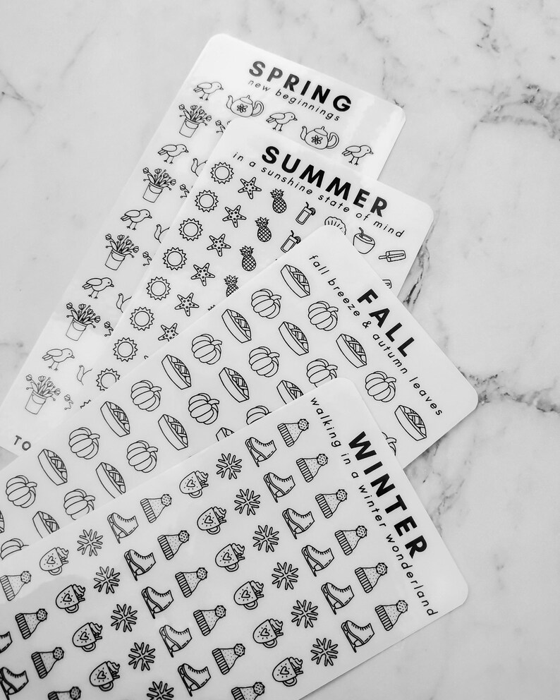 May include: Four sheets of white sticker paper with black outlines of various seasonal icons. The top sheet says "SPRING new beginnings" and features icons like a teapot, birds, and plants. The second sheet says "SUMMER in a sunshine state of mind" and features icons like pineapples, sunglasses, and seashells. The third sheet says "FALL fall breeze & autumn leaves" and features icons like pumpkins, pies, and leaves. The bottom sheet says "WINTER walking in a winter wonderland" and features icons like snowflakes, ice skates, and mugs.
