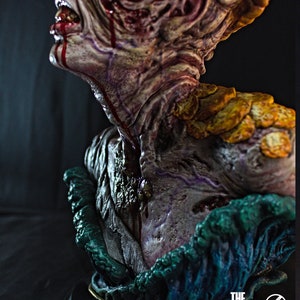 May include: A detailed bust of a creature from "The Last of Us" video game. The sculpture features a grotesque, decaying face with exposed flesh, dripping blood, and fungal growths. The base is dark with the game's logo.