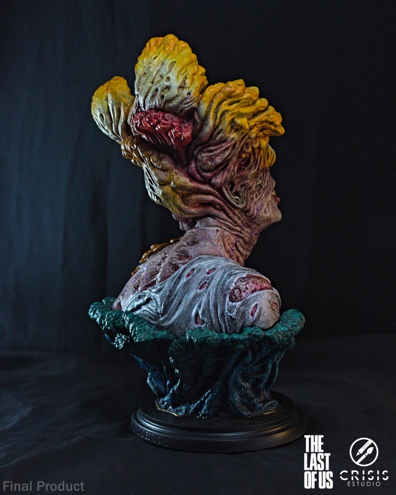 May include: A detailed bust of a Clicker from The Last of Us, featuring a grotesque, fungal head in shades of yellow, red, and brown. The figure has a decaying appearance, with a textured, zombie-like skin and a tattered shirt. The base is black.