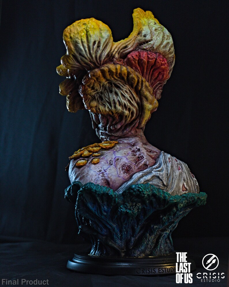 May include: A detailed bust of a Clicker from The Last of Us, featuring a grotesque, fungal head in shades of yellow, orange, and red. The bust has a decaying, textured appearance with a purple and white torso, and is set on a black base.