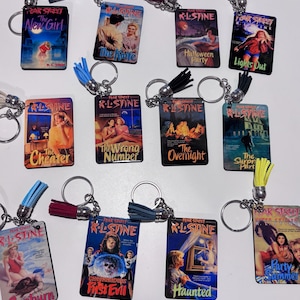 May include: A collection of Fear Street book cover keychains. Each keychain features a different book cover design with titles like "The New Girl", "The Cheater", and "Sunburn". The keychains have silver rings and colorful tassel accents.