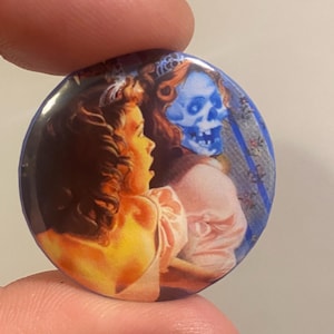May include: A round button featuring a vintage illustration of a woman with a shocked expression, facing a blue-toned skeletal figure. The button has a glossy finish and a dark blue border, with a vintage aesthetic.