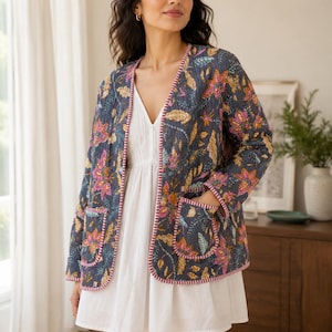 May include: A dark grey quilted jacket featuring a vibrant floral pattern in shades of pink, yellow, and green. The jacket has long sleeves, two front patch pockets, and a distinctive pink and white striped trim along the edges and cuffs.