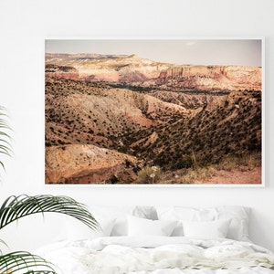 May include: A panoramic view of a desert landscape with layered hills and canyons. The hills are a mix of brown, tan, and red hues, with sparse vegetation. The sky is a pale blue with a few clouds.